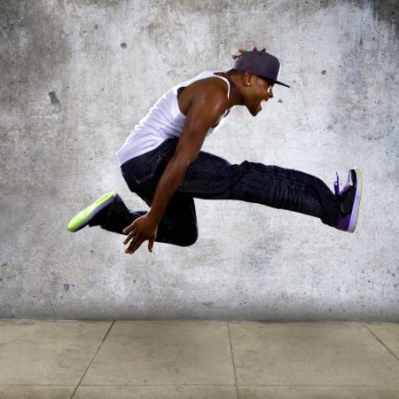 Black urban hip hop dancer jumping high on a concrete background